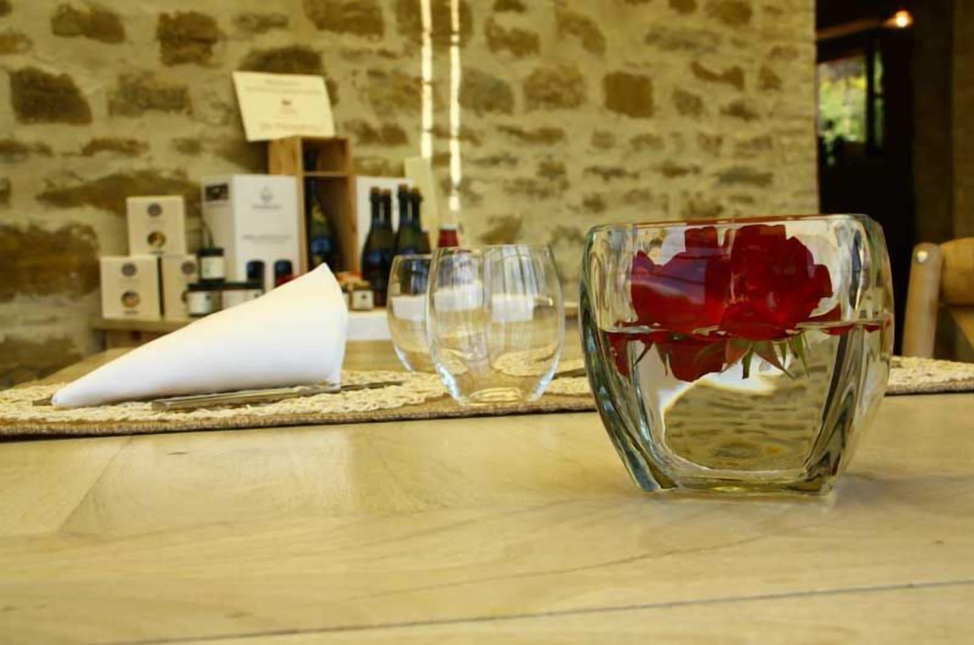 A table with a glass vase containing red roses, a white napkin cone, and two empty wine glasses.