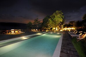 A swimming pool with lounge chairs and a wooden deck, surrounded by trees and night lighting. - La Tavola dei Cavalieri (Assisi)