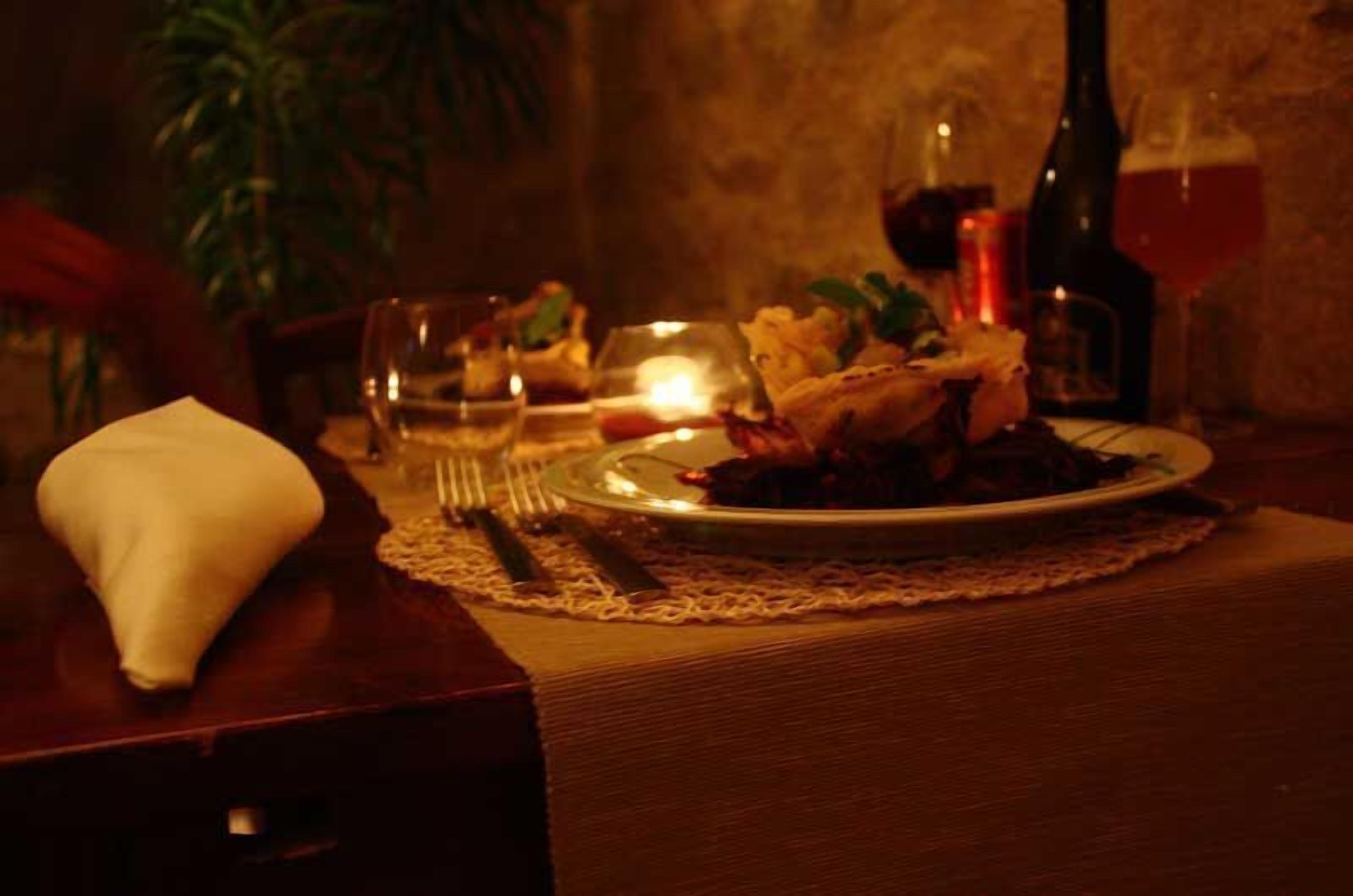 Una mesa de comedor tenuemente iluminada con un plato de comida, una botella de vino y una vela.