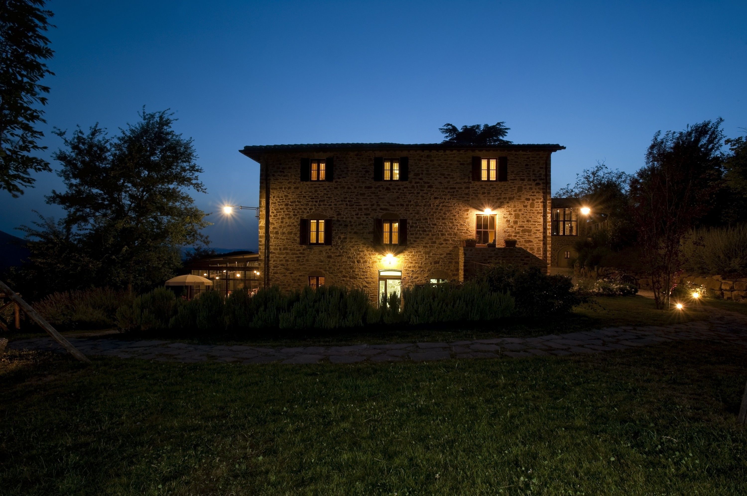 A stone building with multiple windows and a well-lit entrance, surrounded by a grassy area and trees.
