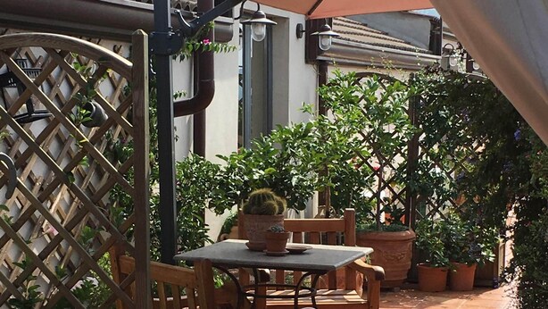 A patio area with a wooden table and chairs, surrounded by potted plants and a lattice fence. - MontAlbano (Caserta)