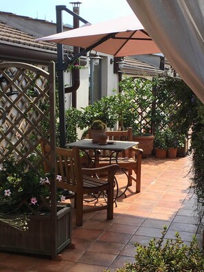 Un patio con mesa y sillas de madera, rodeado de plantas en macetas y un cerramiento tipo celosía.