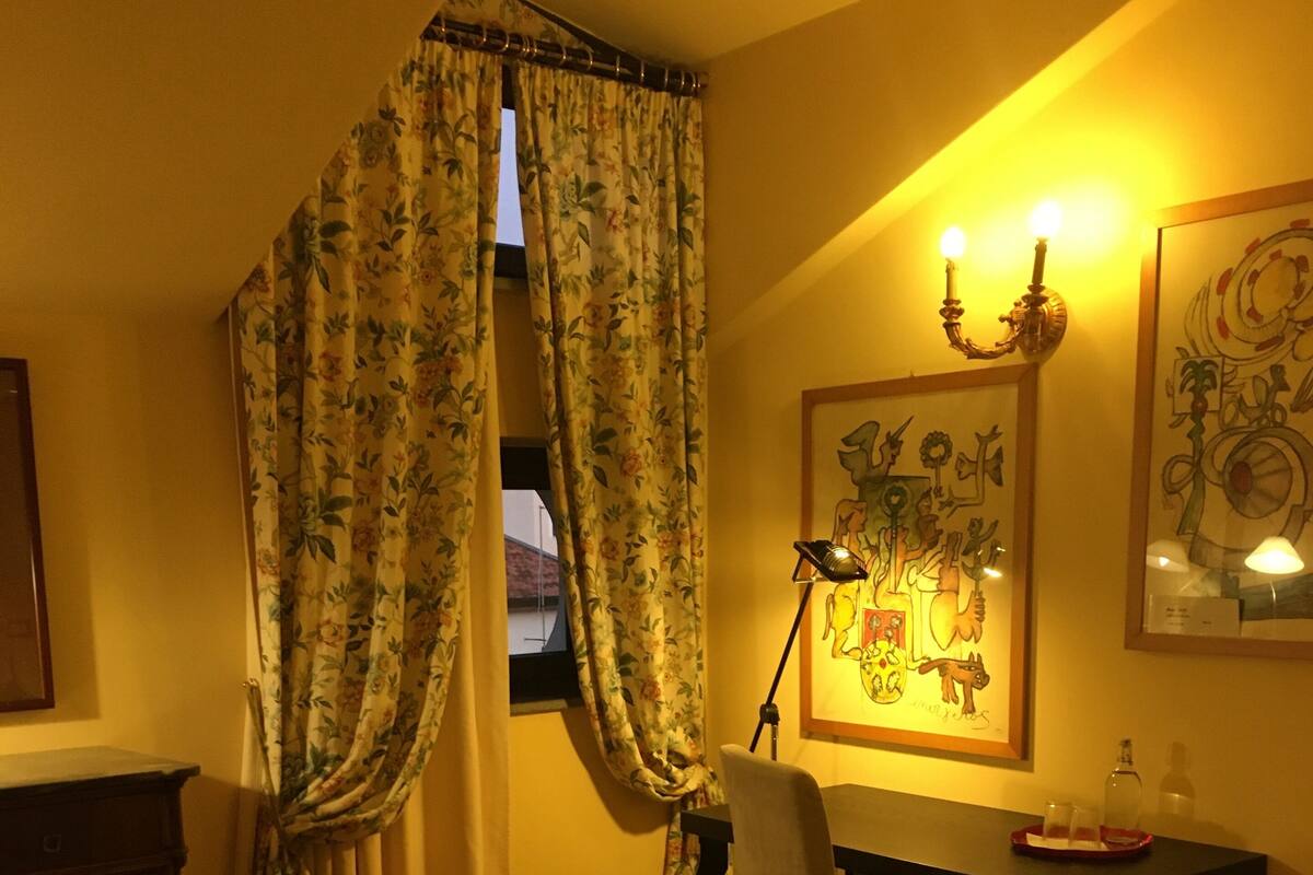 A room with a bed, a desk, a chair, a lamp, and a window with curtains.