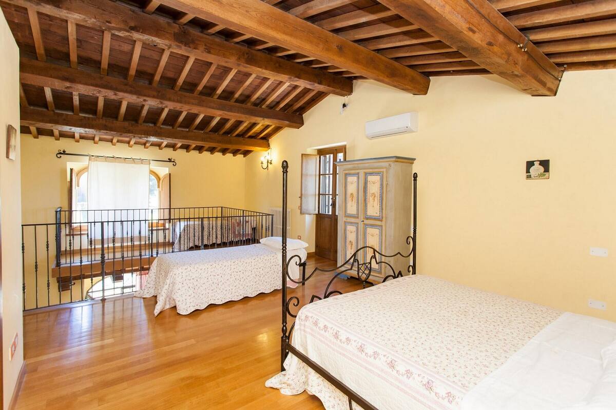 Una camera da letto con due letti, pavimento in legno, un balcone e un soffitto rustico.