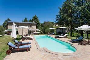 A swimming pool with lounge chairs and umbrellas, surrounded by a stone building and trees. - Podere Caldaruccio La Pineta (Perugia)
