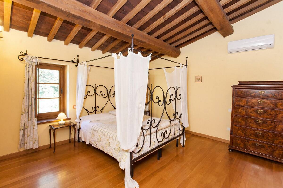 Un letto a baldacchino con tende bianche, un comò in legno e una finestra con tende.