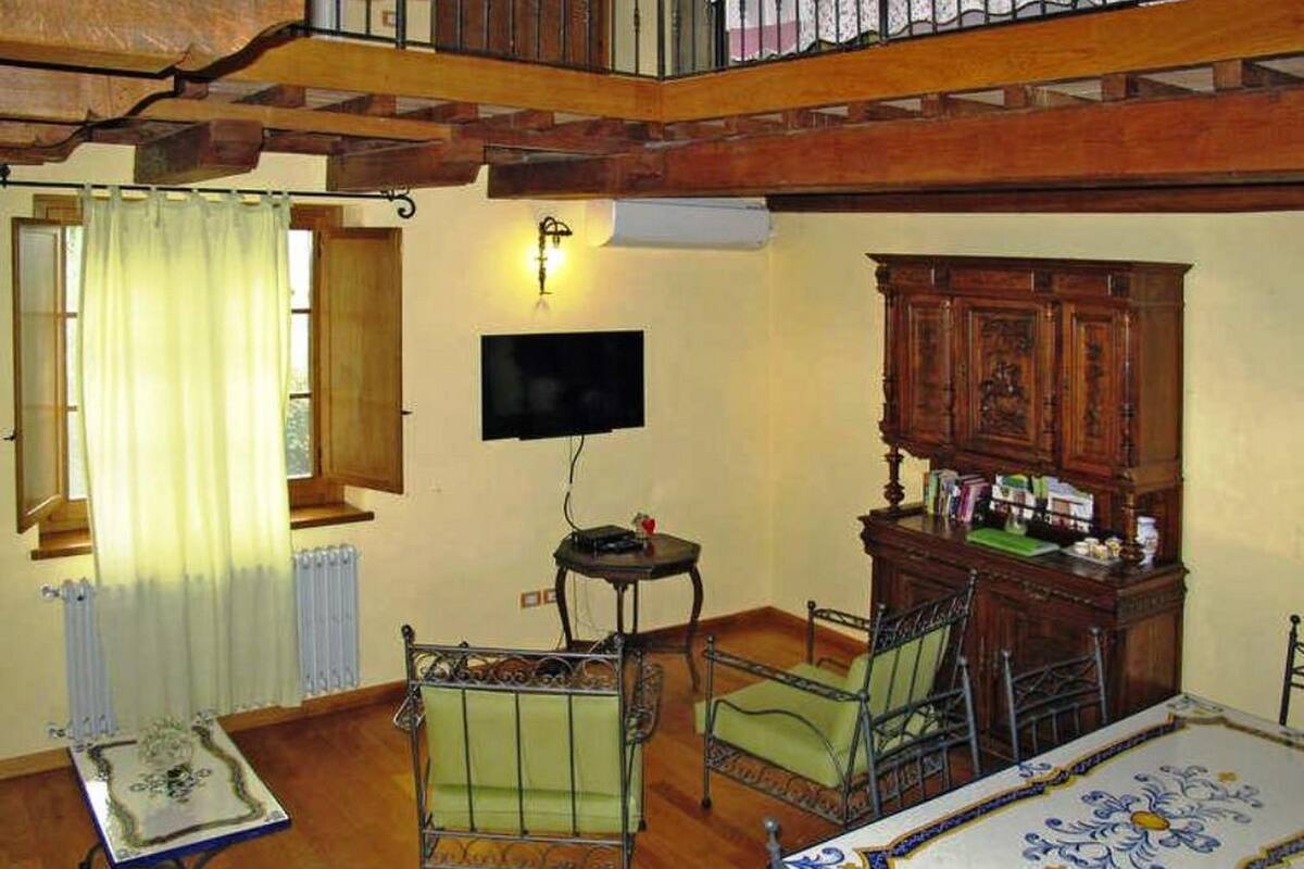 Una stanza con pavimento in legno, una poltrona rivestita in verde, un tavolino, un mobile contenitore con libri e una televisione fissata al muro.