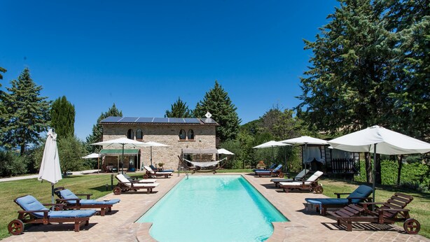 A swimming pool with lounge chairs and umbrellas, surrounded by a stone building and trees. - Podere Caldaruccio La Pineta (Perugia)