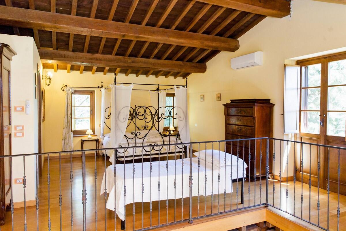 Camera da letto con soffitto in legno, un letto con struttura in metallo, una cassettiera in legno e una finestra con tende.