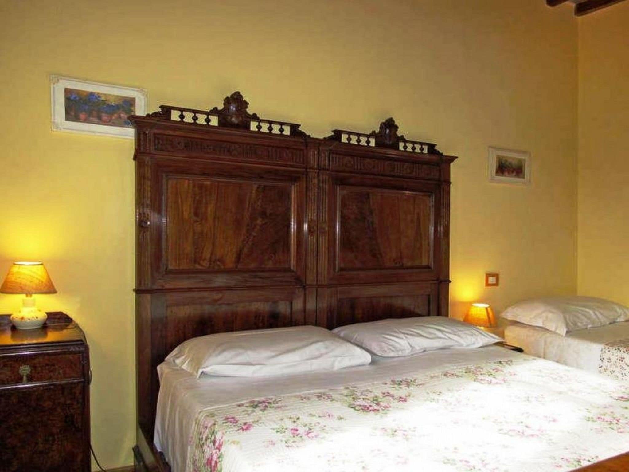 A bedroom with a wooden wardrobe, two bedside tables with lamps, and a floral bedspread.