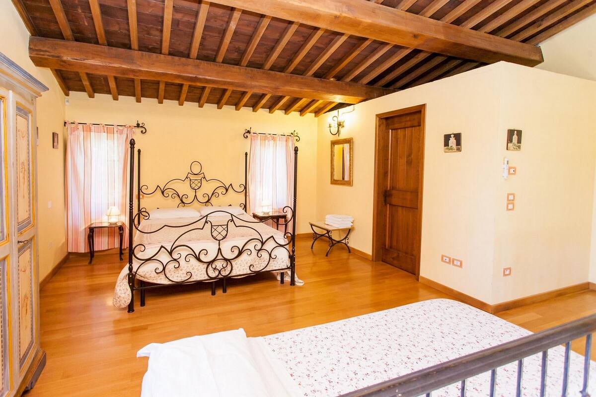 Una camera da letto con soffitto in legno, un letto a baldacchino, un comodino e una sedia.