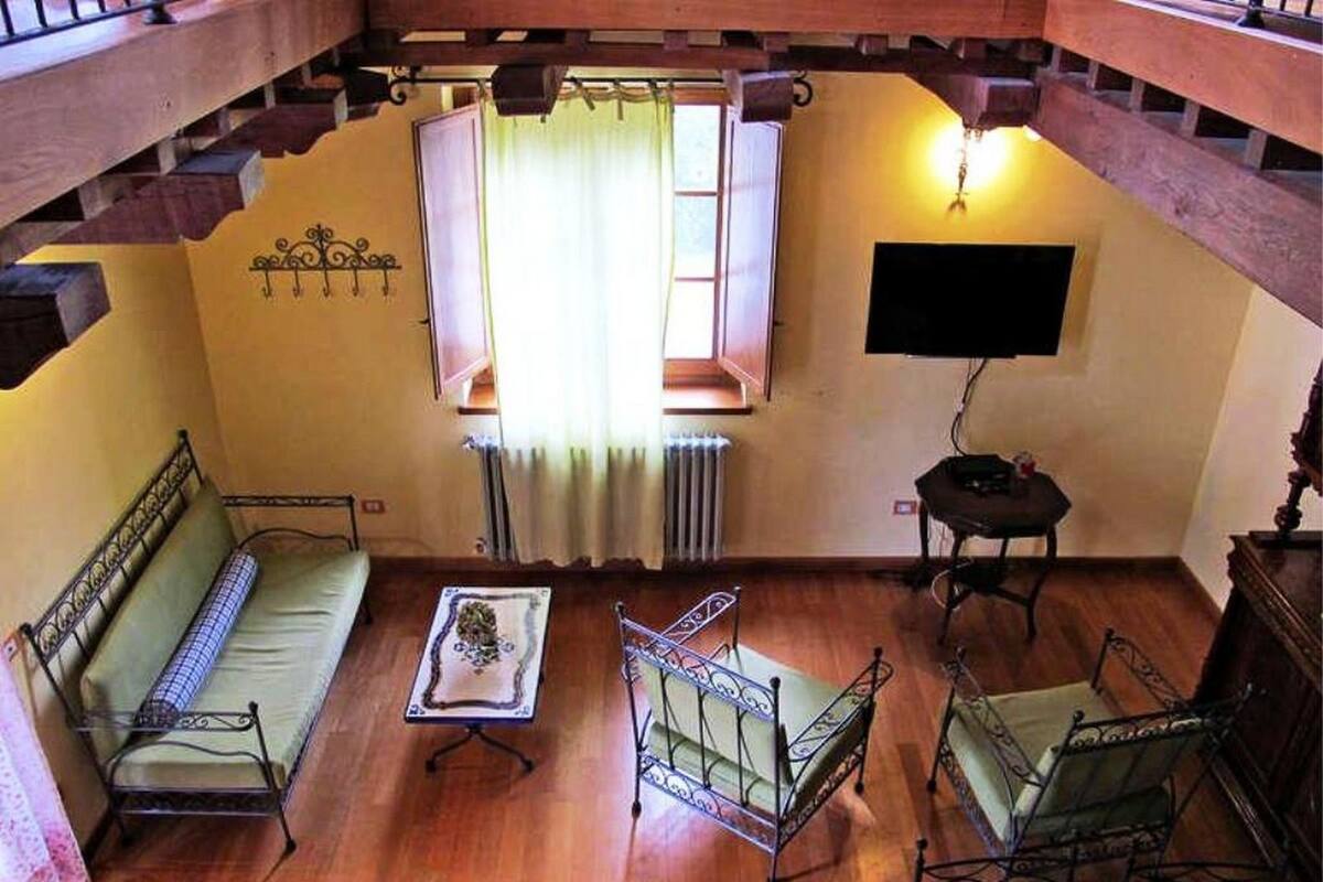 Una stanza con pavimento in legno, un divano, un tavolino, una sedia, un termosifone e una televisione a parete.