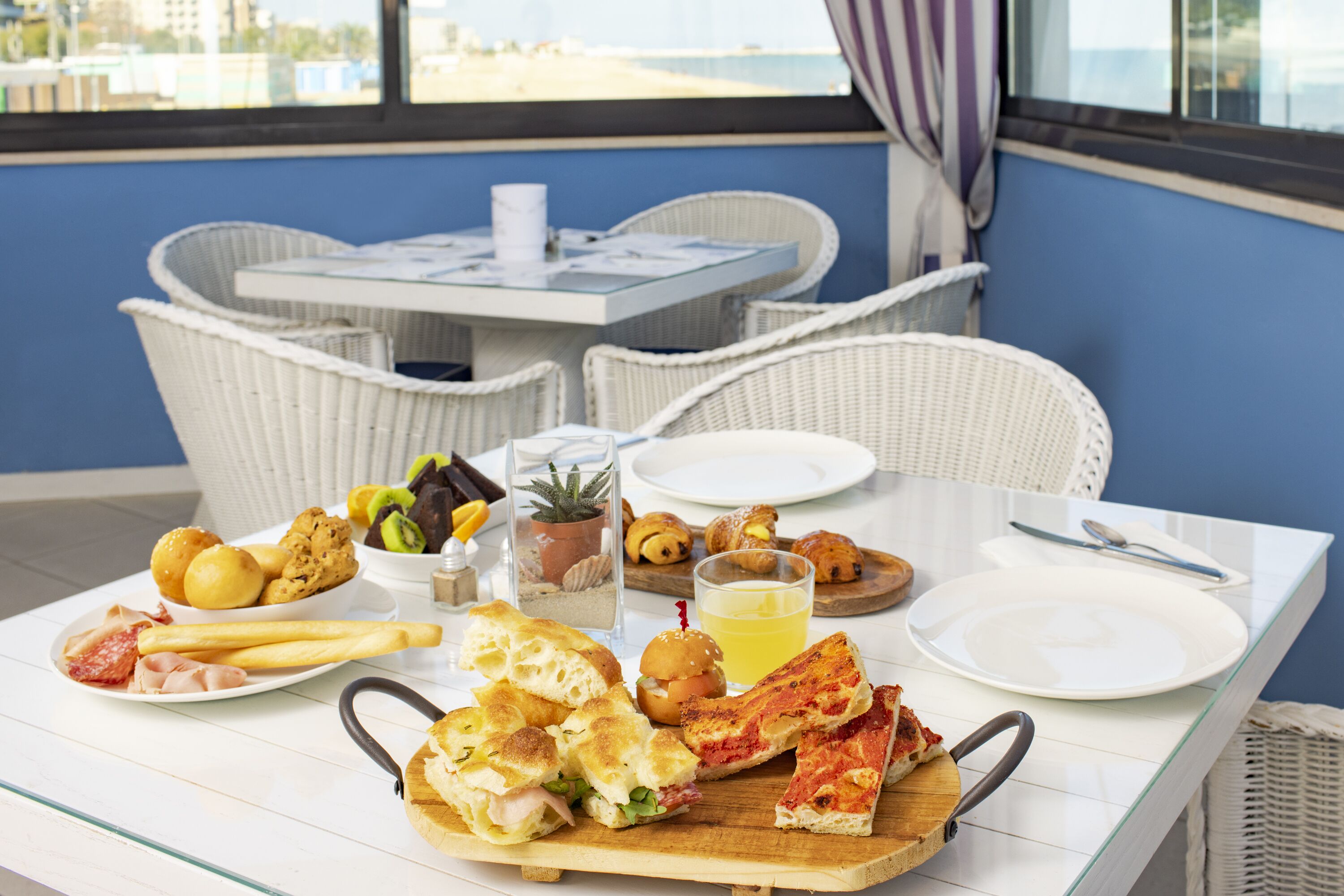 A dining table with various food items, a glass of juice, and a view of the city in the background.