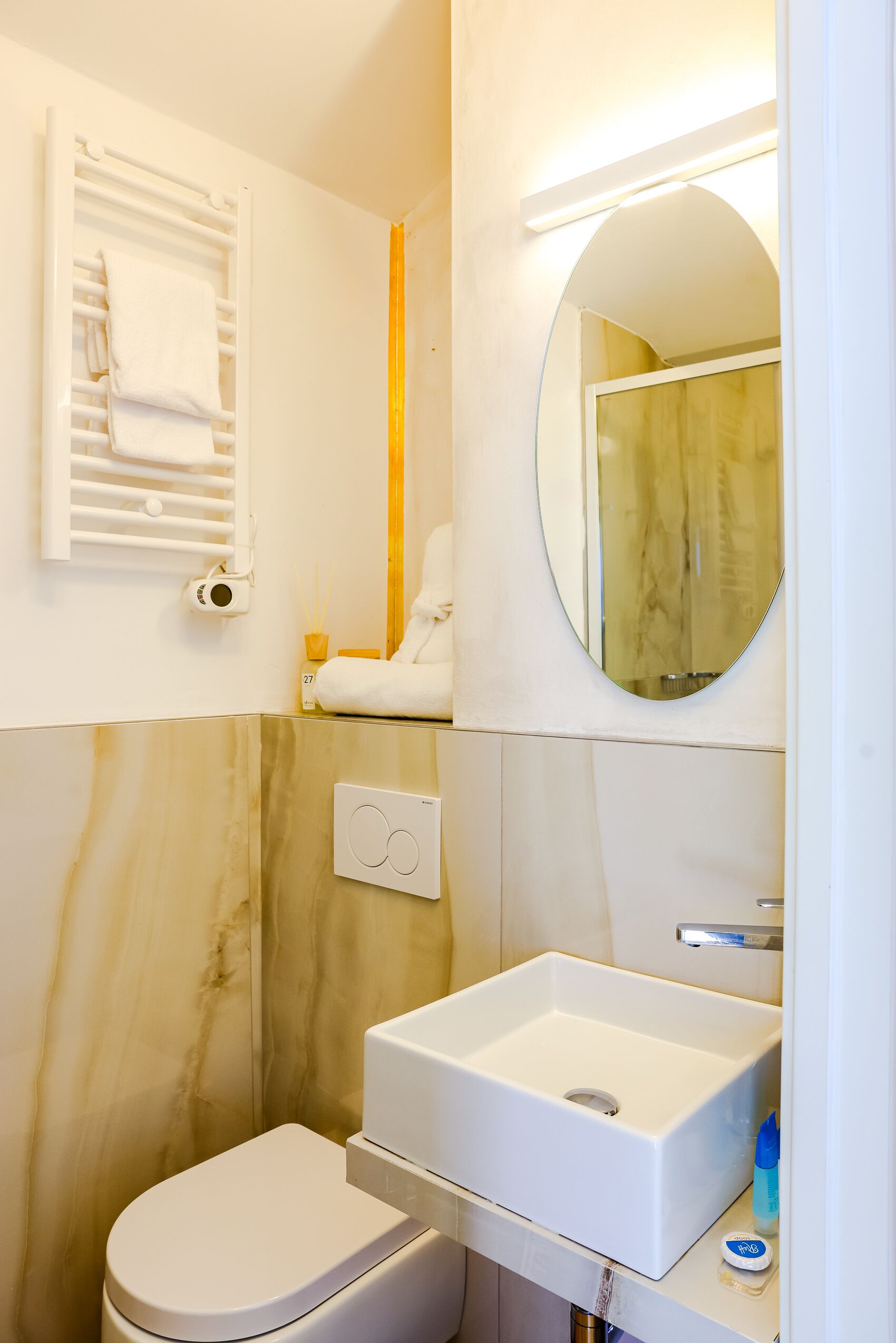 Un baño con lavamanos blanco, inodoro, toallero, espejo y dispensador de toallas.