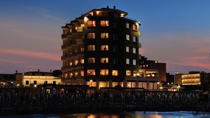 Un hotel de varios pisos con balcones, vista al agua y una zona de piscina con sombrillas.