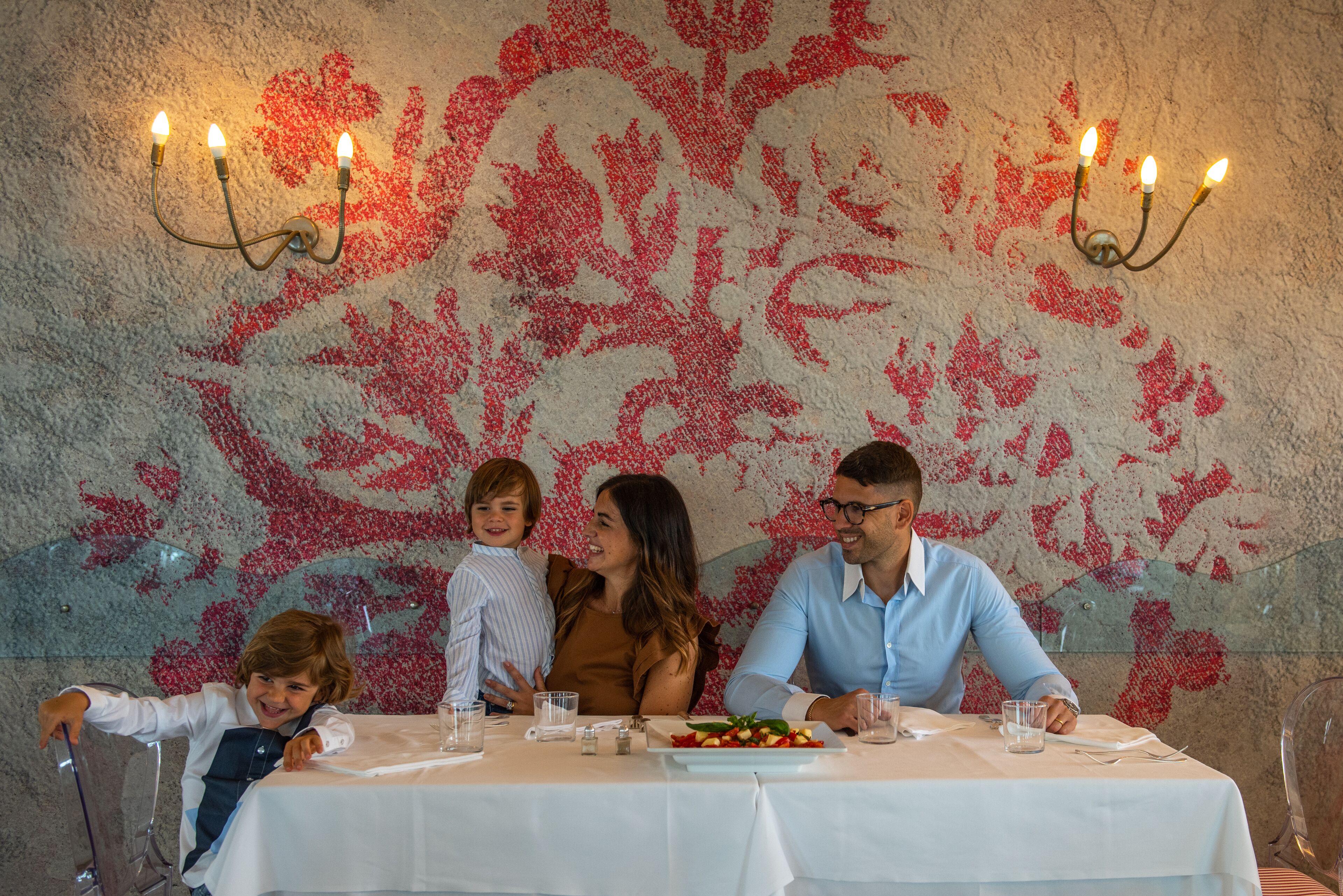 A family dining at a table with a floral wall mural and candelabra lighting.