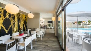 A modern indoor area with white furniture, a large window overlooking a pool, and a wall with a tree design. - Hotel Eden Garda (Garda)
