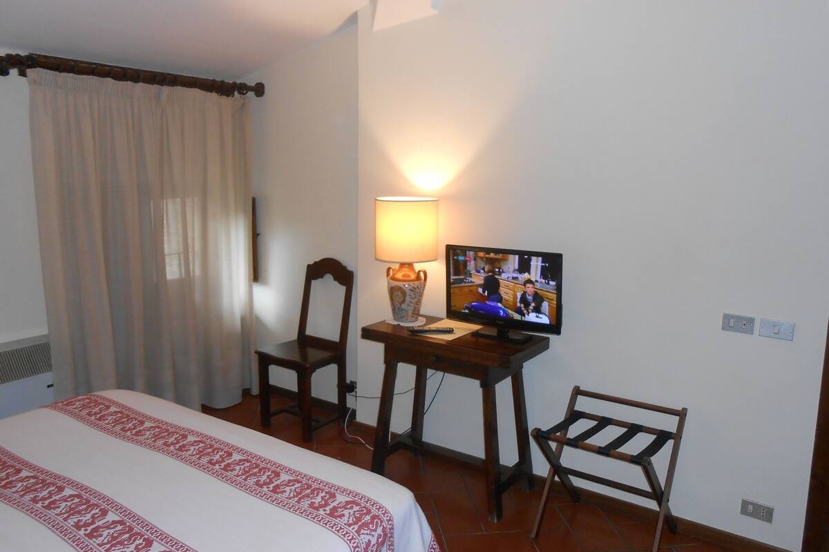 A hotel room with a bed, a desk with a lamp, a television, and a chair.