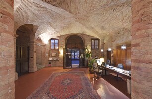 Un vestíbulo amplio con un alto techo abovedado de ladrillo, una alfombra grande y decorativa, y un mostrador de recepción con sillas.