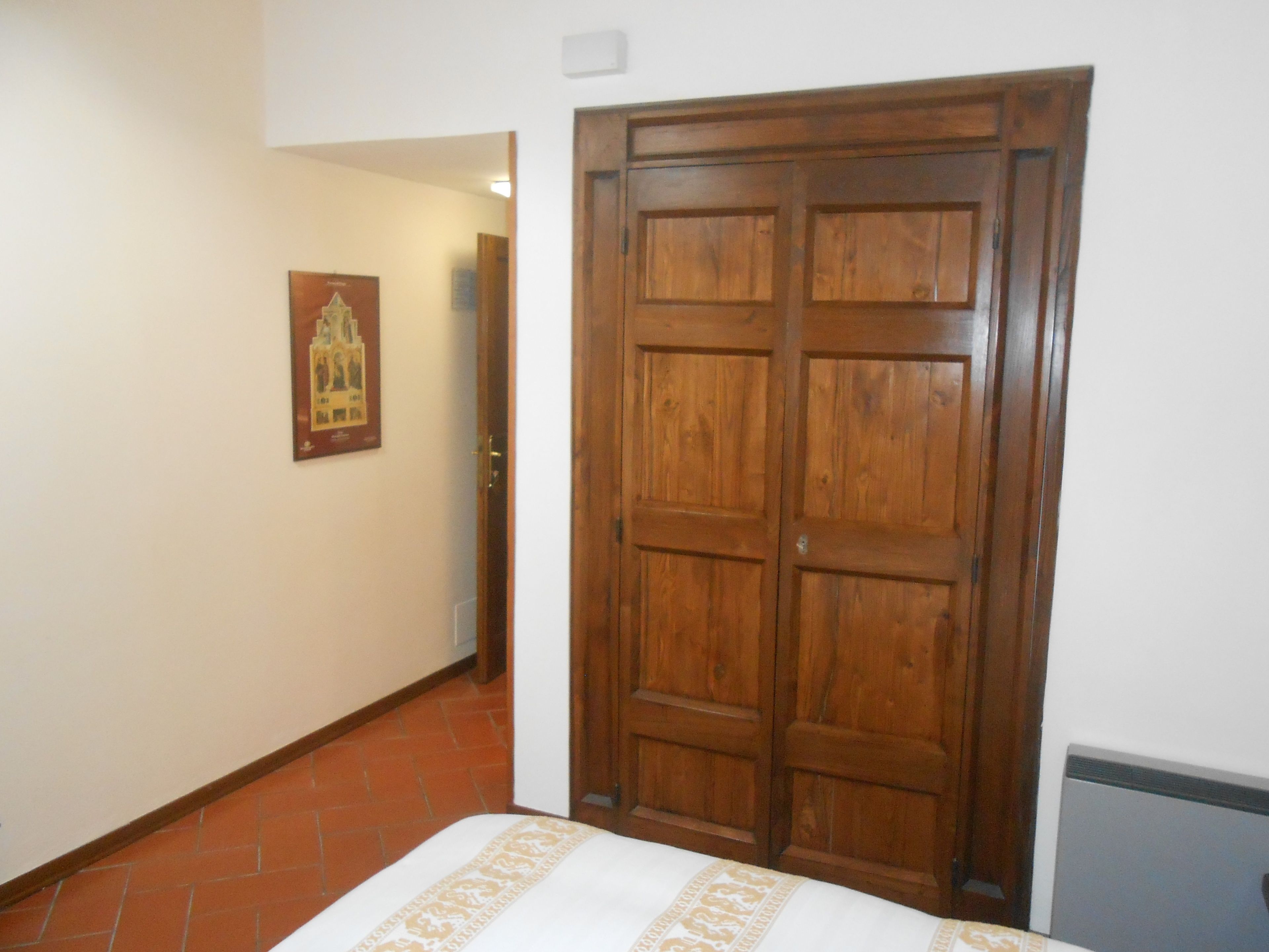 A hallway with a wooden door, a tiled floor, and a framed picture on the wall.