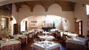 A spacious dining area with multiple tables set for guests, featuring a rustic brick ceiling and a large arched doorway leading to a kitchen area. - Lo Spedalicchio (Bastia Umbra)