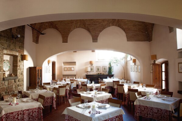 Un comedor amplio con varias mesas dispuestas para los huéspedes, que presenta un techo de ladrillo rústico y un gran arco de entrada a una zona de cocina.