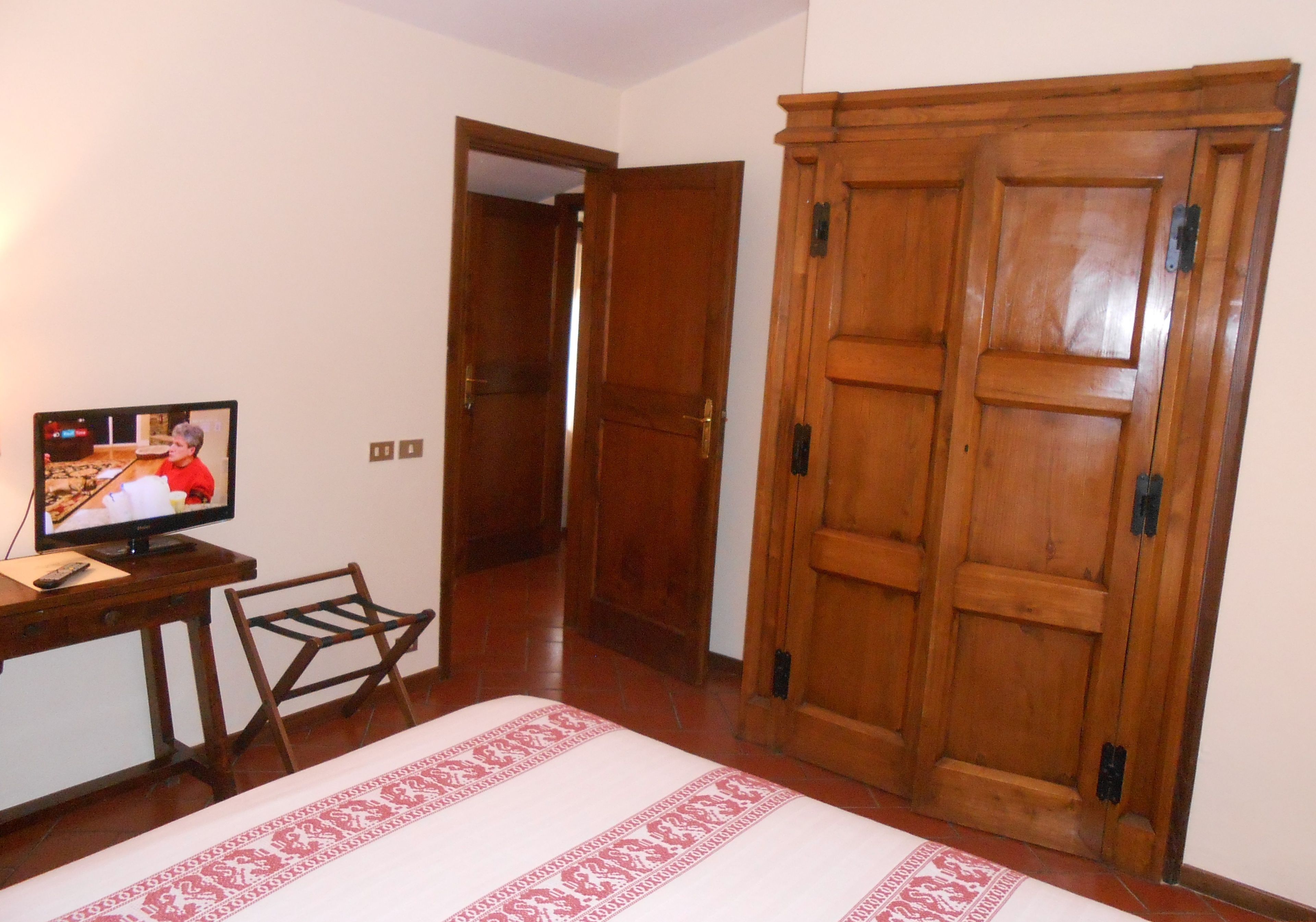 Una stanza con un letto, un'armadietto in legno, una televisione su una scrivania e una sedia.