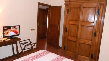 Una stanza con un letto, un'armadietto in legno, una televisione su una scrivania e una sedia.