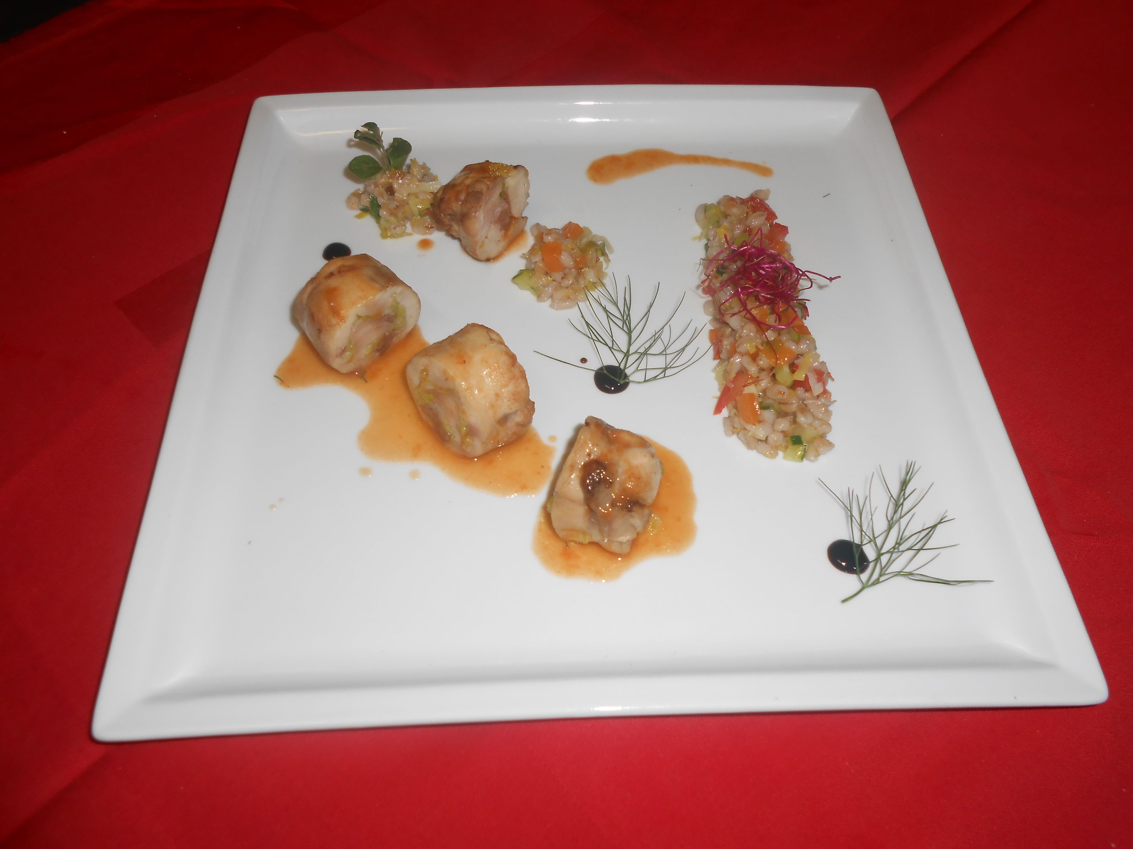 Un piatto quadrato bianco con diversi cibi, tra cui gnocchi e un'insalata, su una tovaglia rossa.