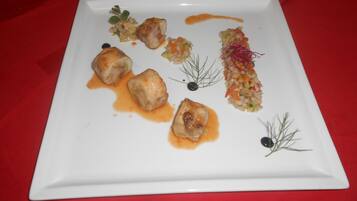 Un piatto quadrato bianco con diversi cibi, tra cui gnocchi e un'insalata, su una tovaglia rossa.
