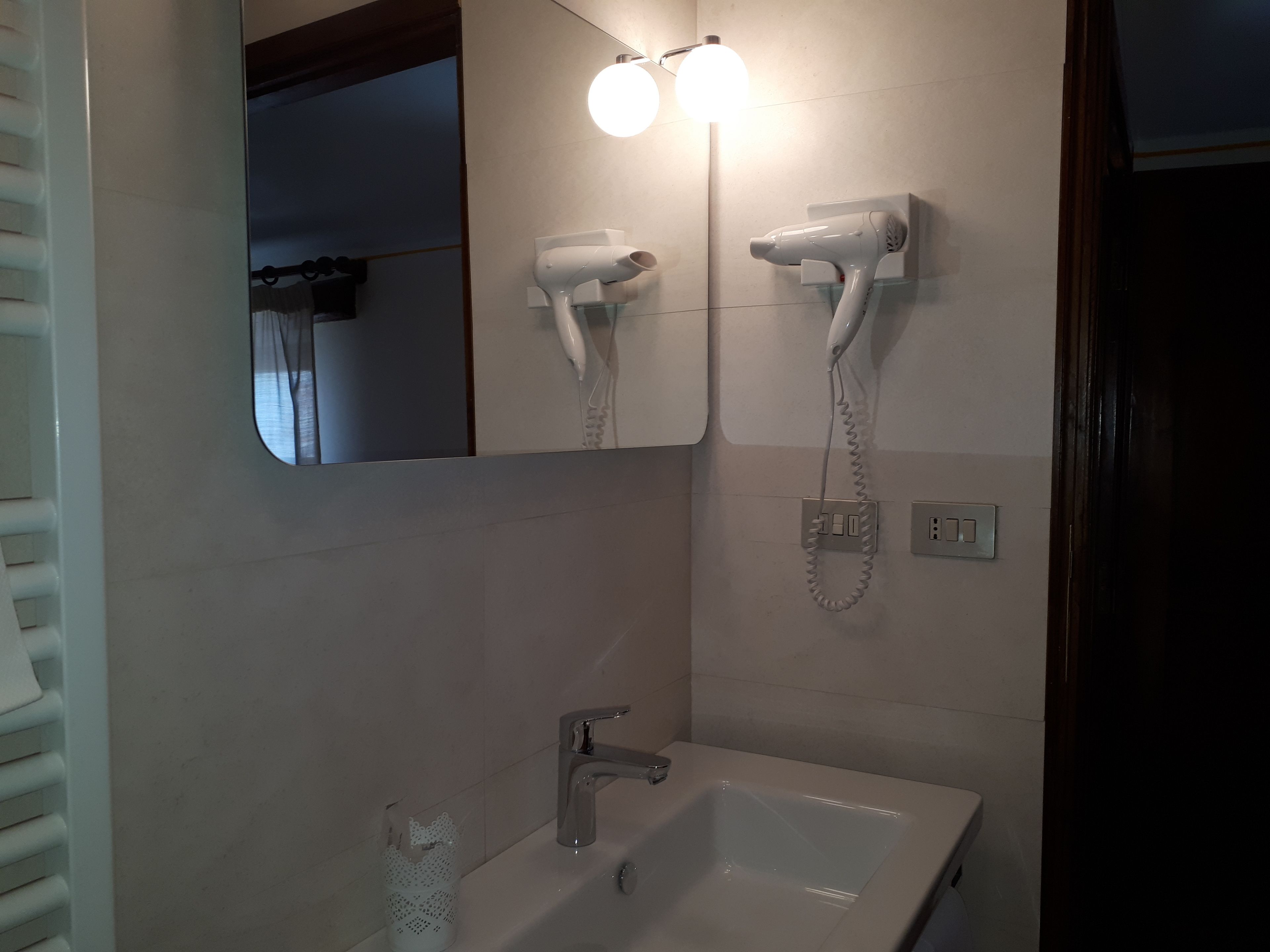 A bathroom with a sink, two hair dryers mounted on the wall, and a mirror above the sink.