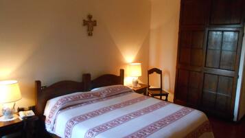 Una habitación de hotel con una cama, lámparas de noche, una puerta de madera y una cruz en la pared.