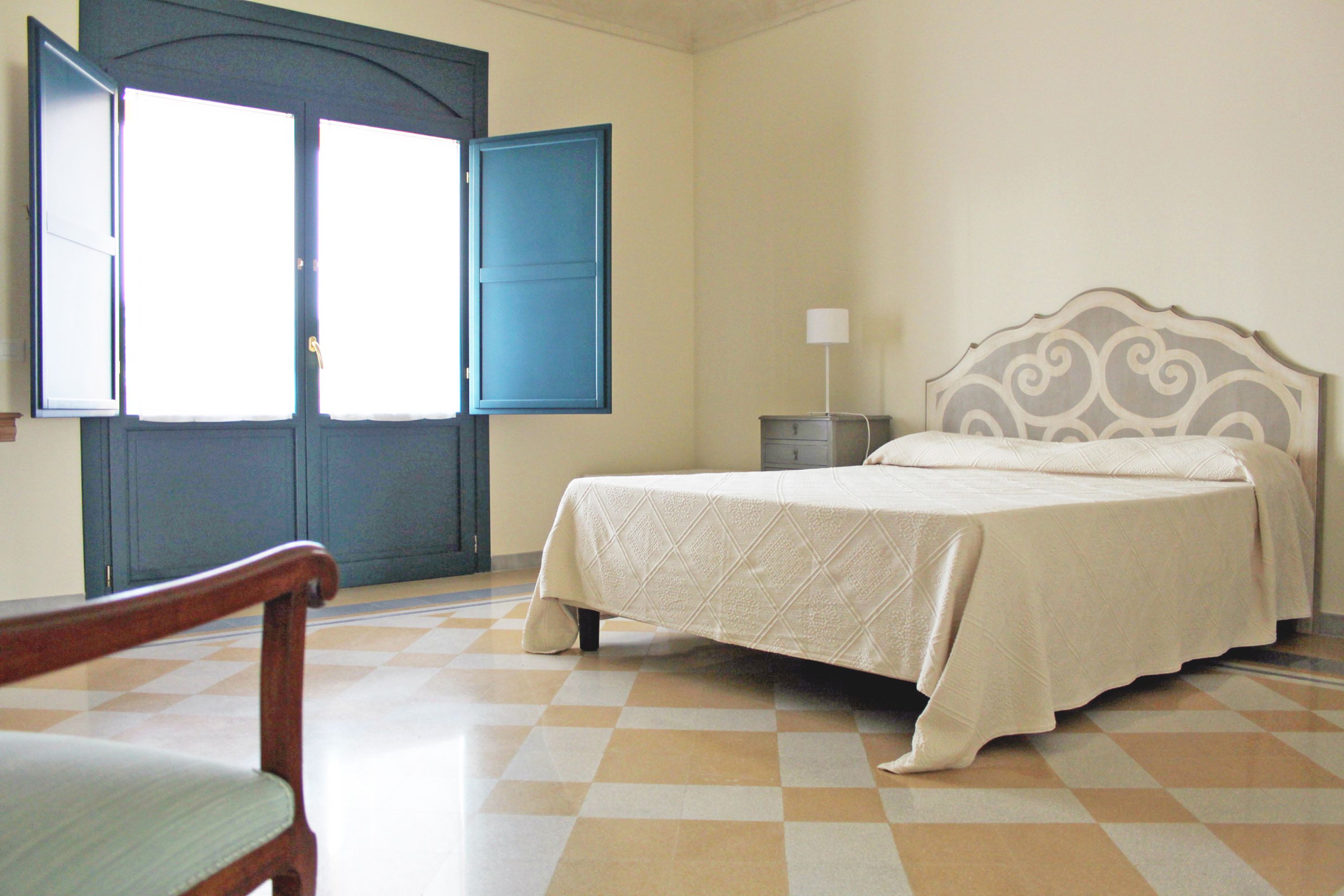 A bedroom with a bed, a chair, a nightstand, and a window with a blue door.
