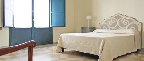 A bedroom with a bed, a chair, a nightstand, and a window with a blue door.