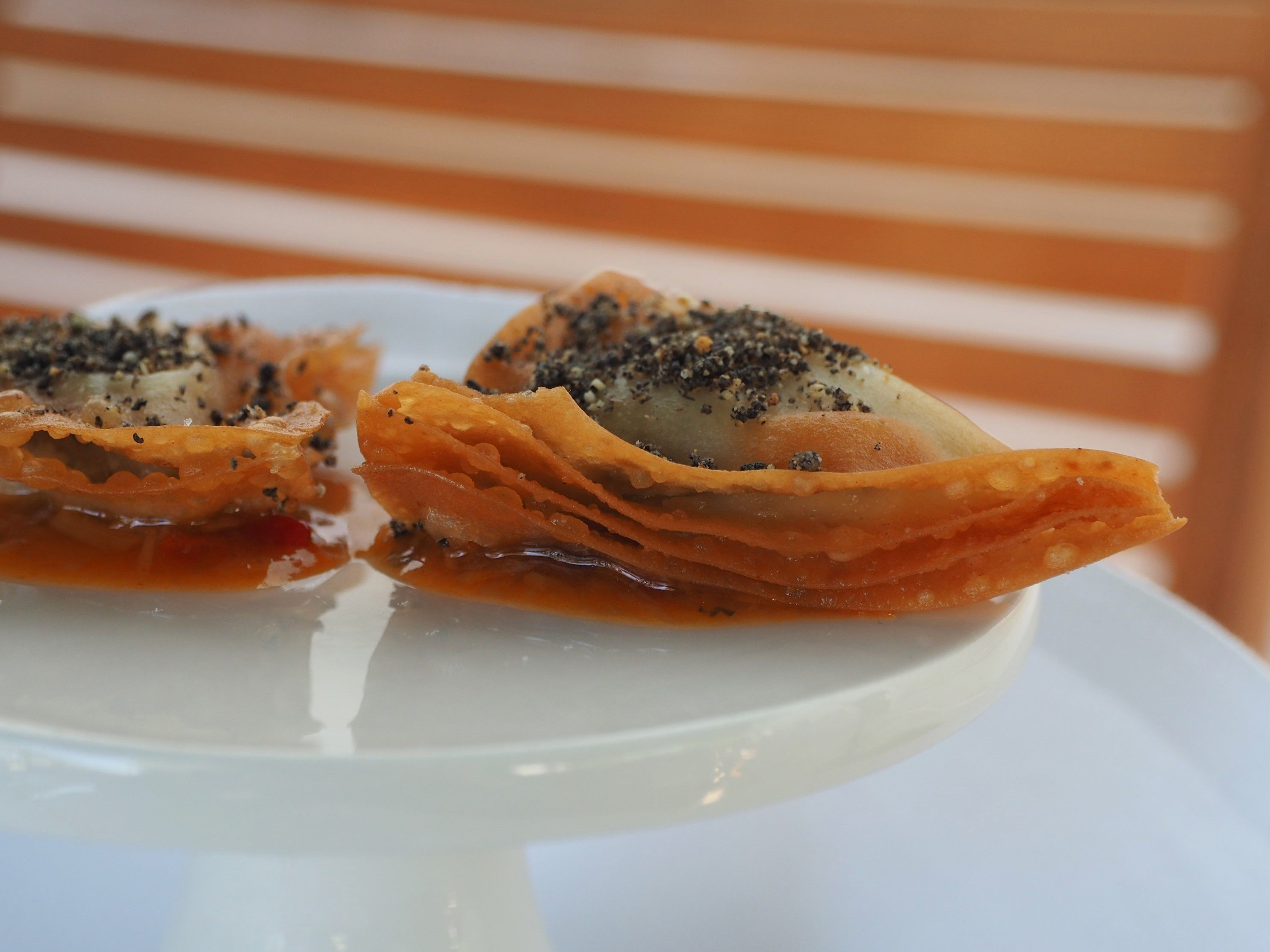 A dessert with a crispy, golden-brown crust, possibly a type of pastry or tart, garnished with black seeds and a red sauce.