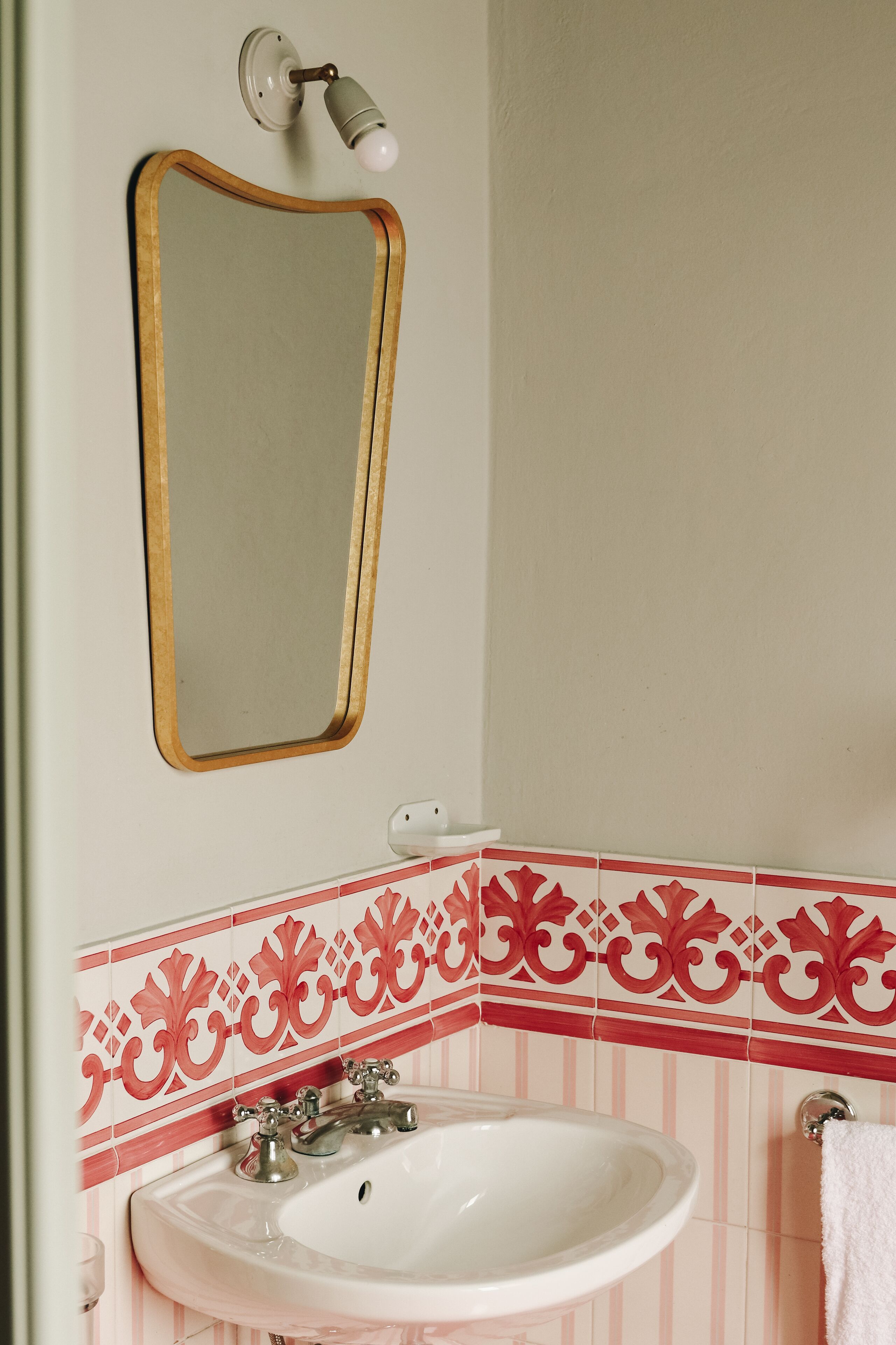 Un baño con un lavamanos blanco, un espejo con marco de madera y baldosas decorativas rojo y blanco.