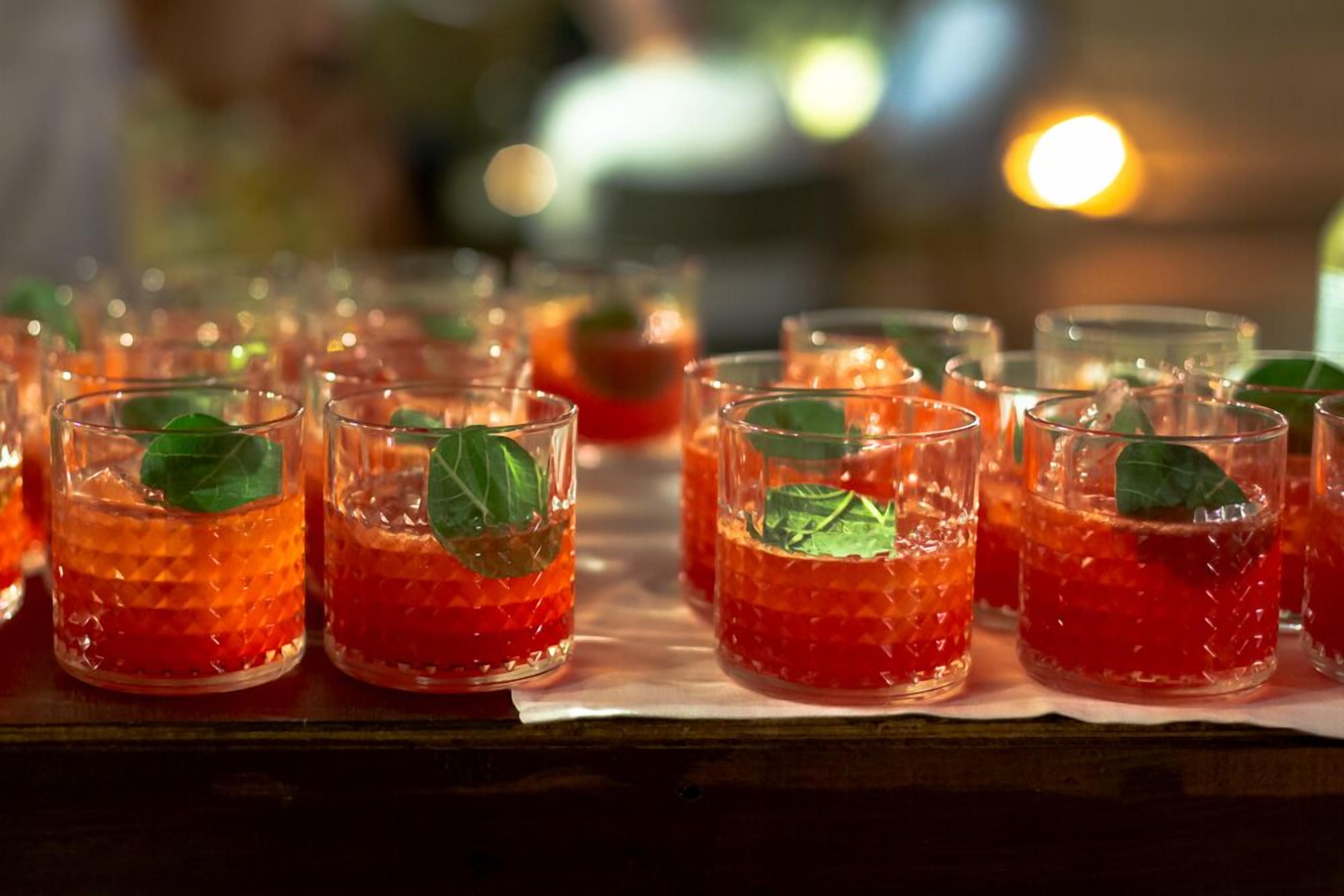 A row of glasses filled with a red beverage, garnished with a green leaf, on a wooden surface.