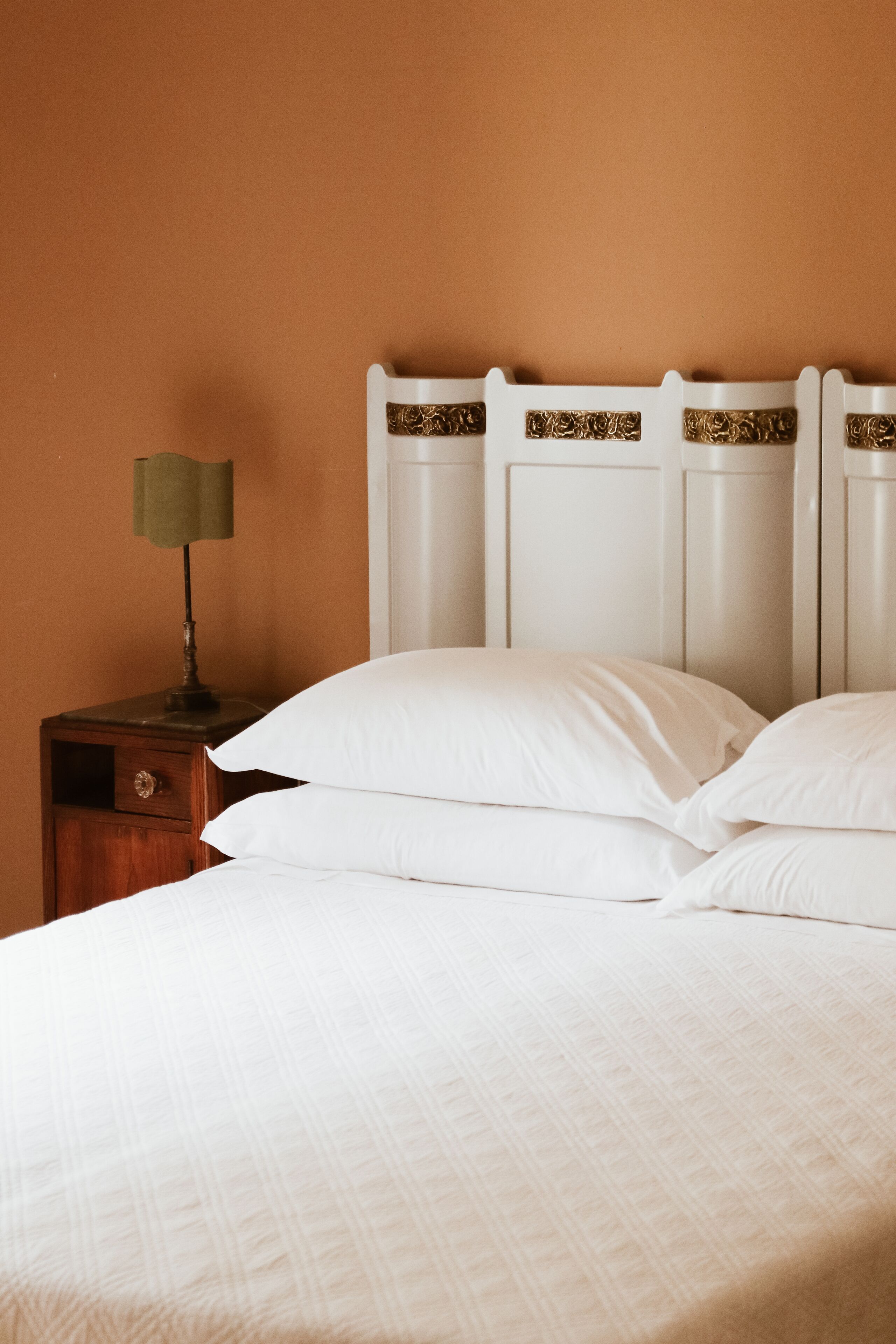A neatly made bed with white linens and a wooden nightstand with a lamp.