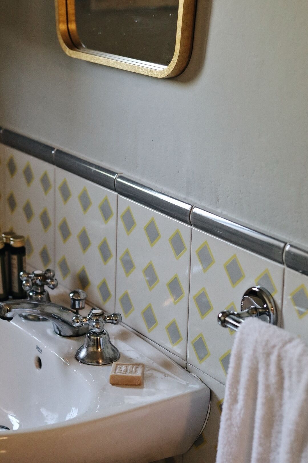 A bathroom with a white sink, two faucets, a mirror, and patterned tiles.