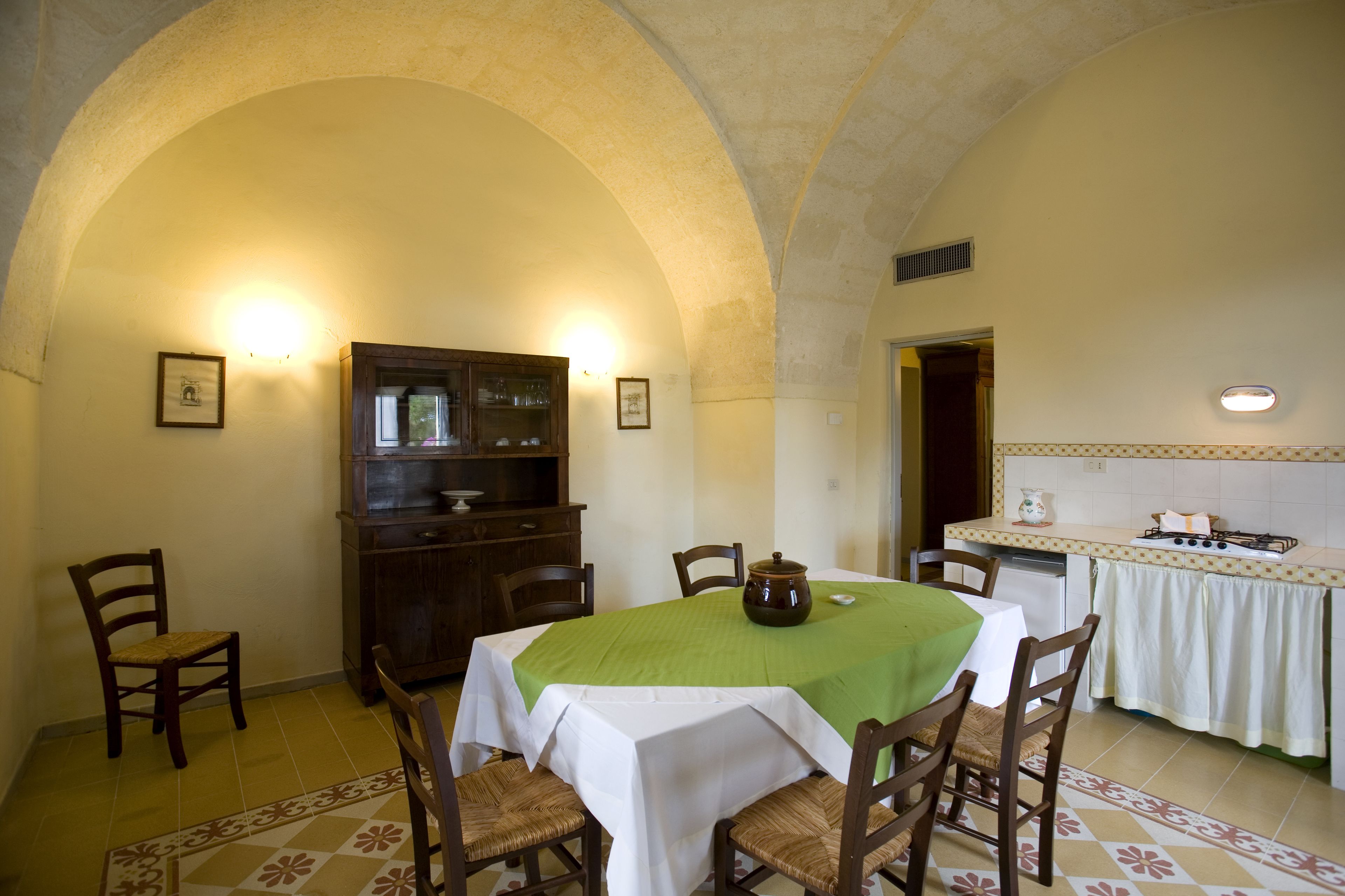 A dining area with a table set for four, surrounded by wooden chairs. An arched ceiling and a cabinet with glass doors are visible.