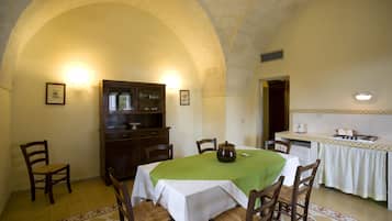 A dining area with a table set for four, surrounded by wooden chairs. An arched ceiling and a cabinet with glass doors are visible.
