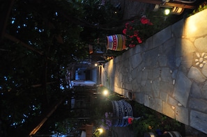 A stone pathway with decorative lights and hanging ornaments, surrounded by lush greenery and flowers. - Villa Mata (Ios)