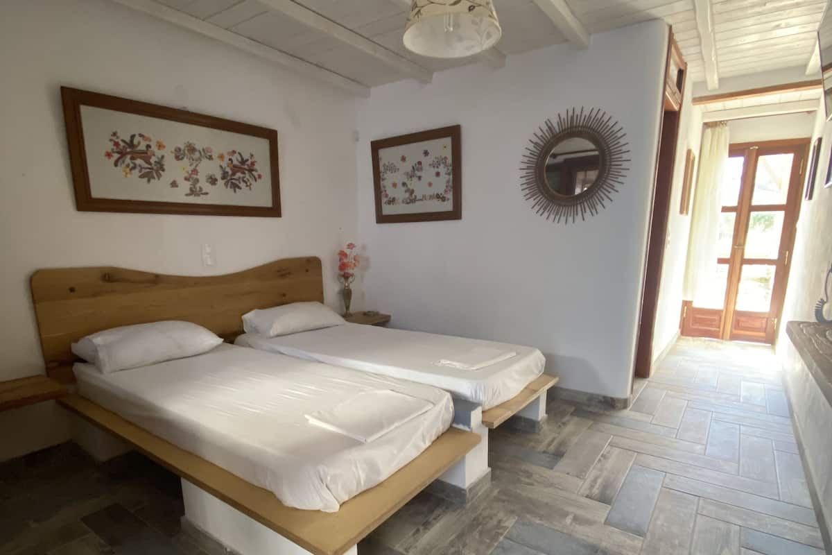 A room with two beds, wooden flooring, a ceiling fan, and framed floral artwork.