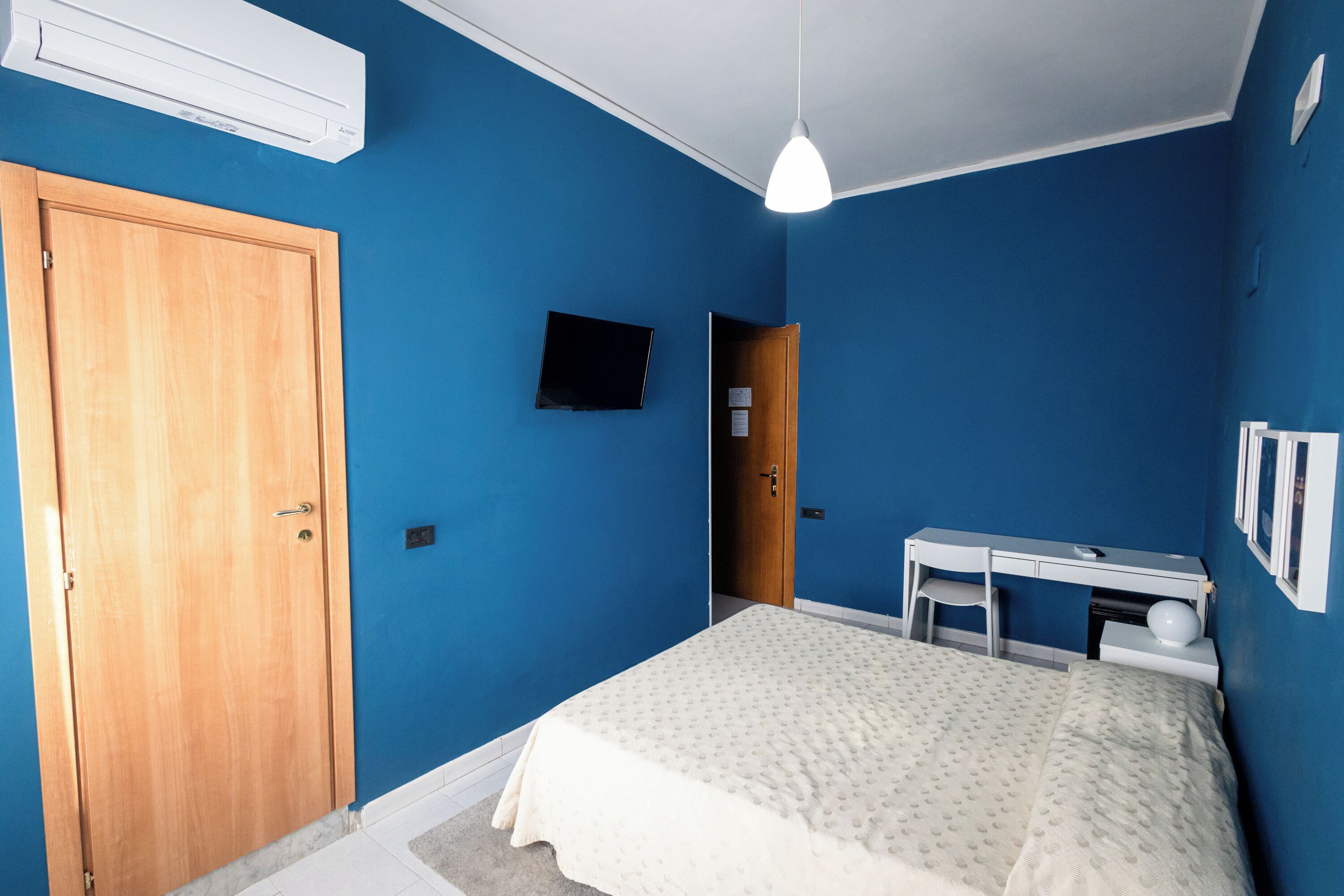 A bedroom with a bed, a desk, a chair, a wardrobe, and a television.