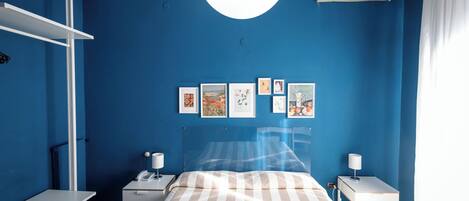 Un dormitorio con cama, mesitas de noche, un escritorio y aire acondicionado instalado en la pared.