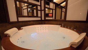 Uma banheira de hidromassagem grande e oval, com borda de madeira e painel de controle lateral.