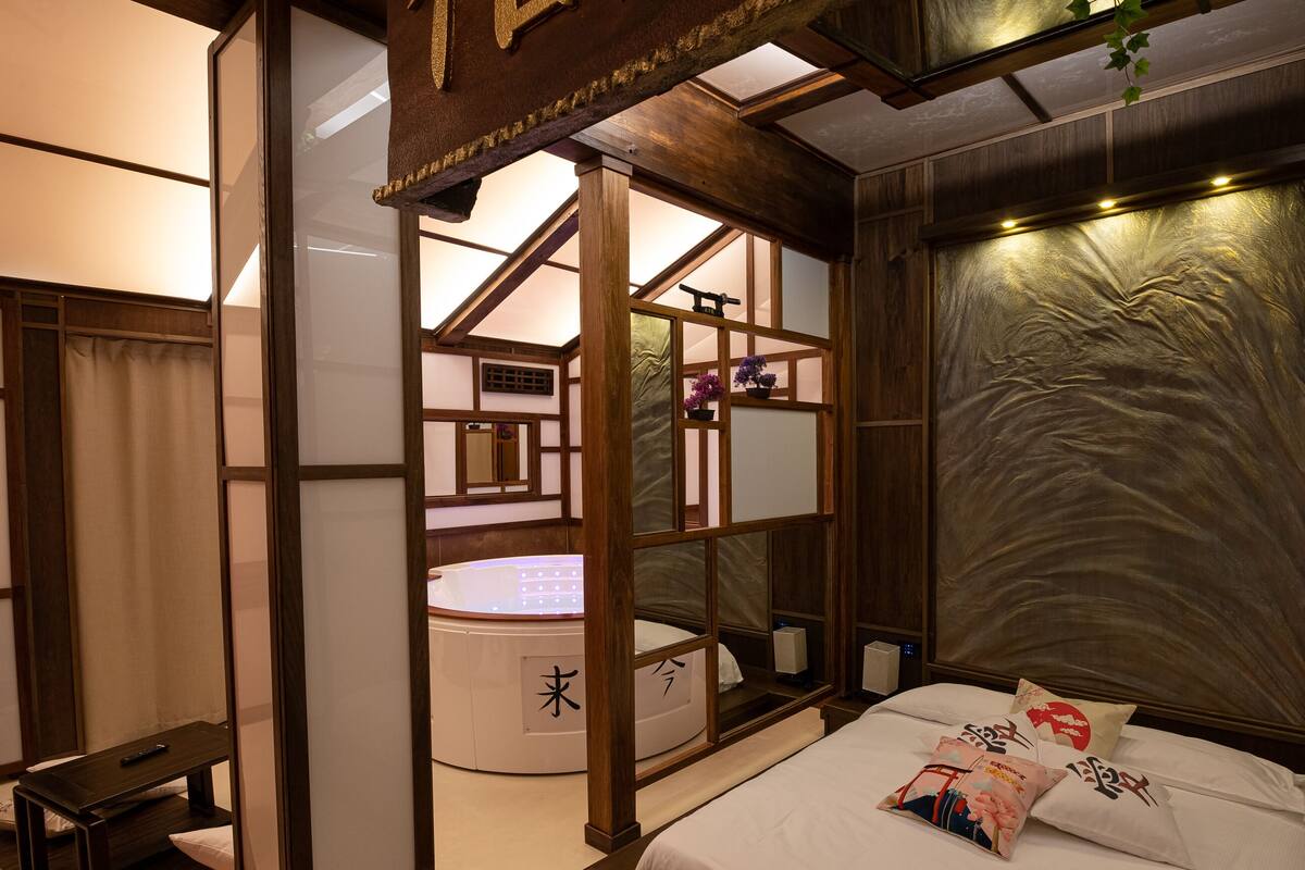 A traditional Japanese-style bedroom with tatami flooring, a shoji screen, a futon bed, and a small washbasin.