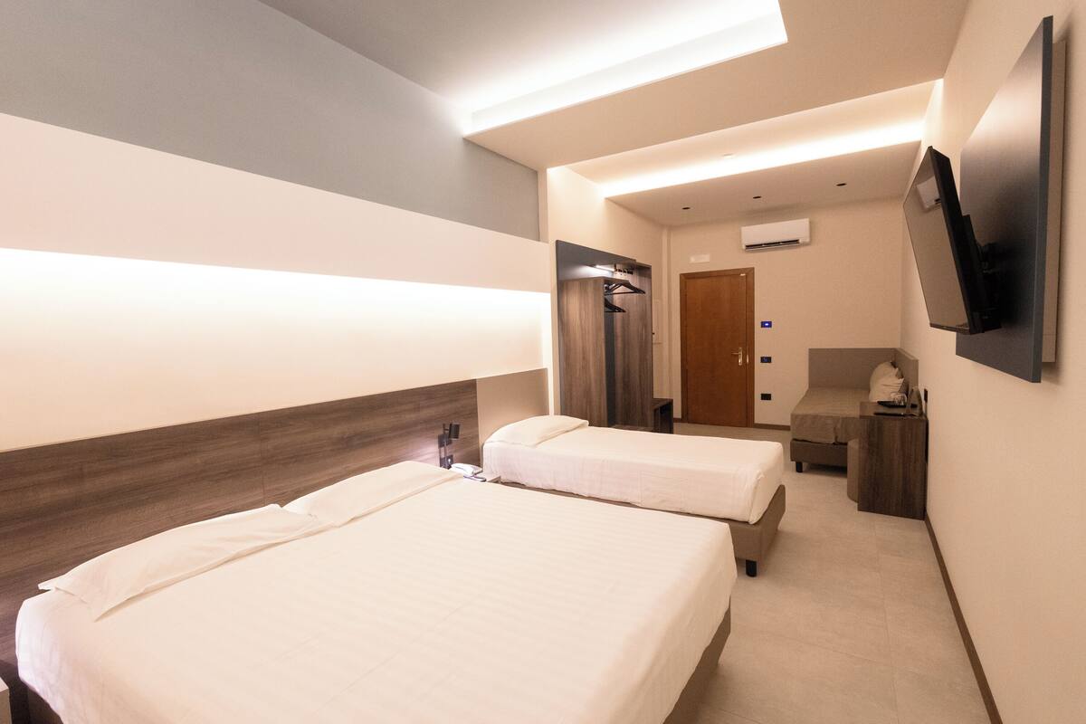 A hotel room with two beds, a TV mounted on the wall, and a small desk with a chair.