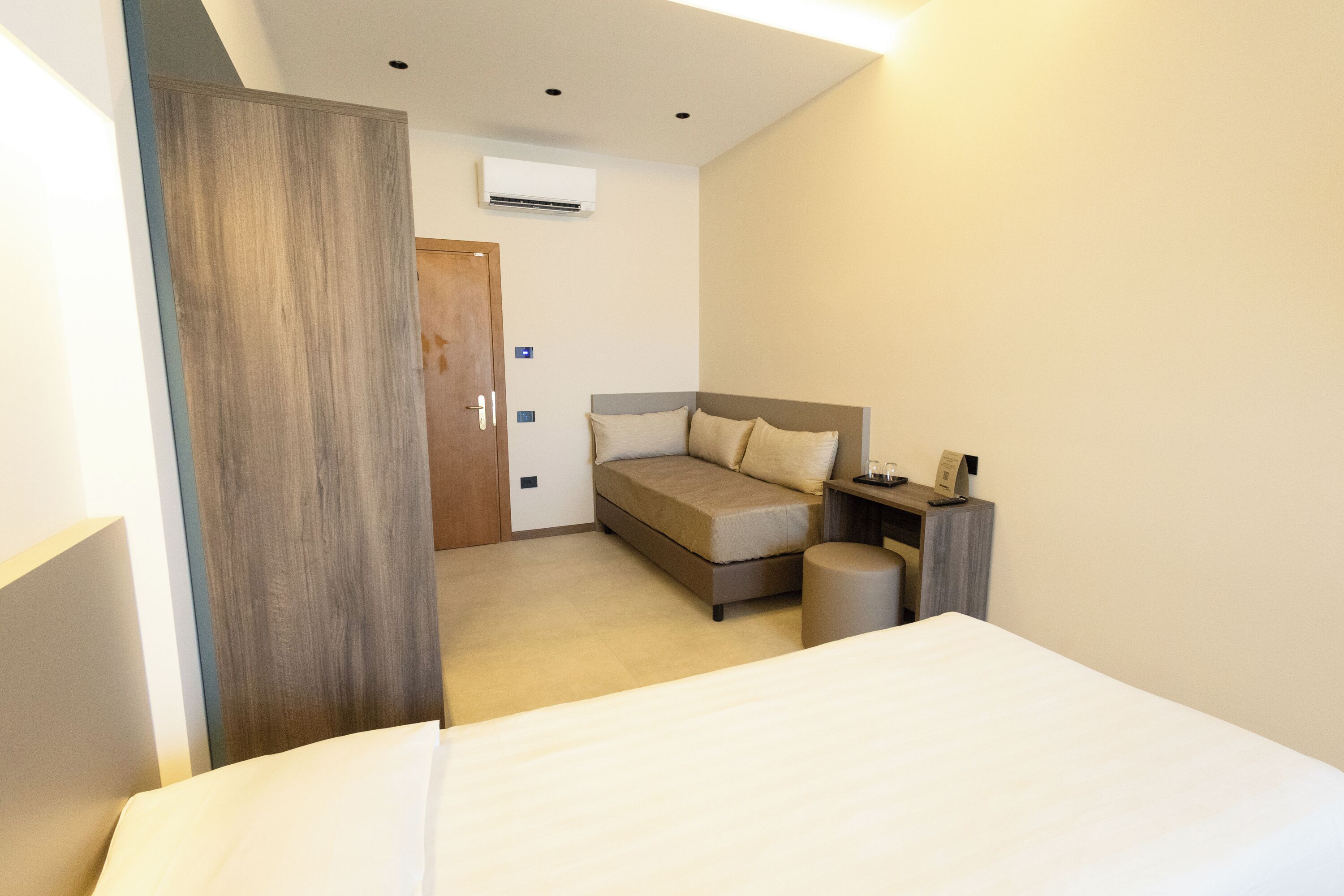 A hotel room with a bed, a sofa bed, a desk, and a wardrobe.