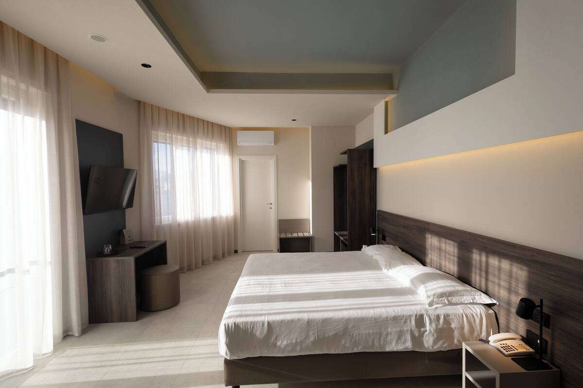 A modern hotel room with a large bed, a desk, a flat-screen TV, and a wardrobe.